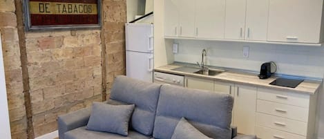 Un espacio habitable compacto con sofá, una pequeña cocina y una pared de ladrillo.