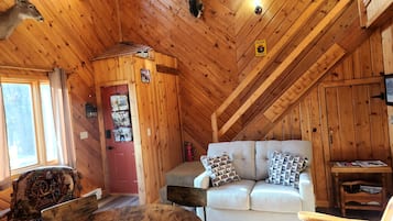 A cozy cabin interior with a wooden ceiling, a red door, a white sofa, and a rustic chair.