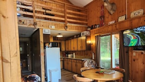 Interior rústico de una cabaña con cocina, comedor y televisor montado en la pared.