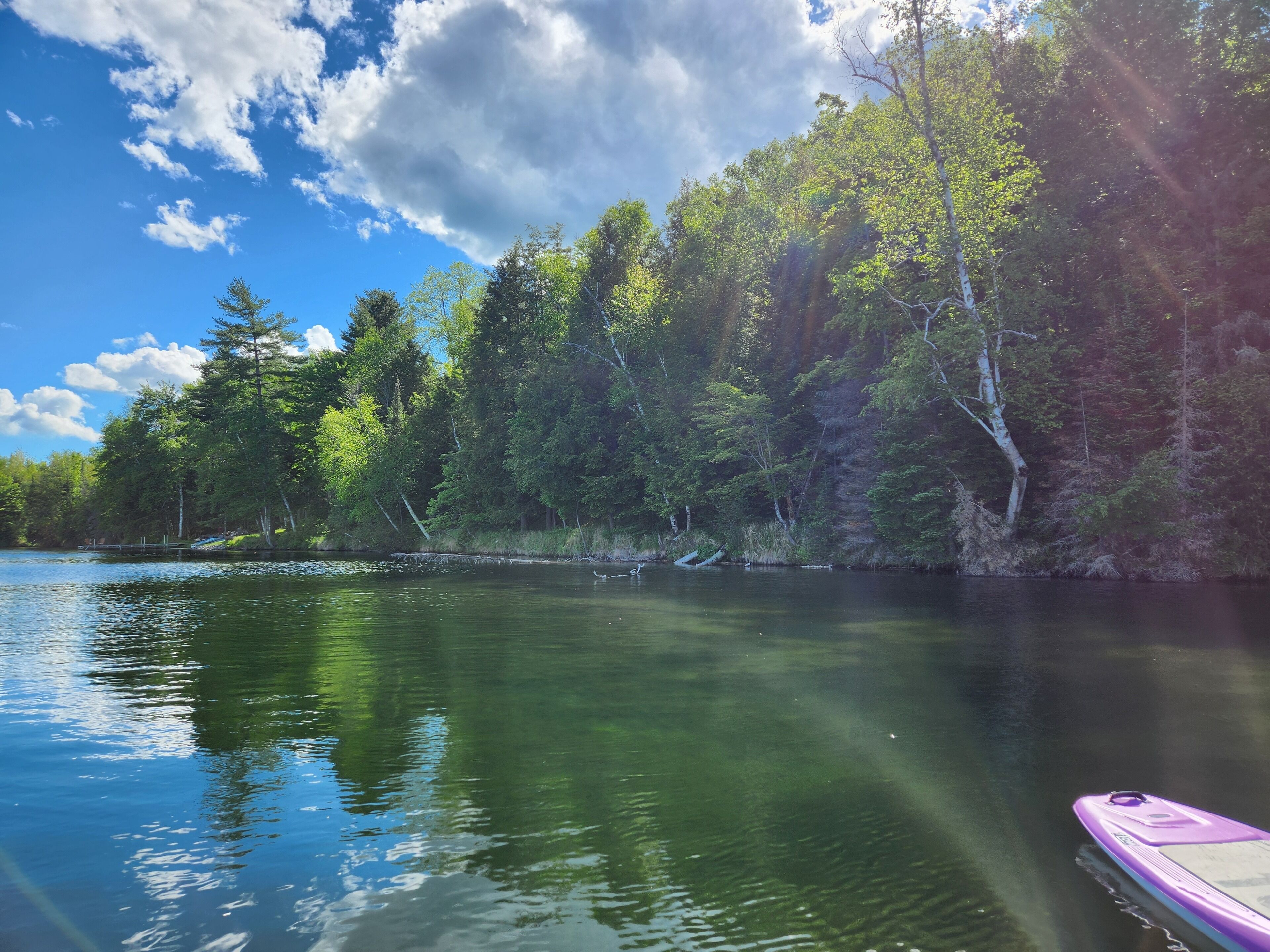 Un lac paisible où flotte un bateau à rames, entouré d’une forêt dense et surplombé d’un ciel dégagé.