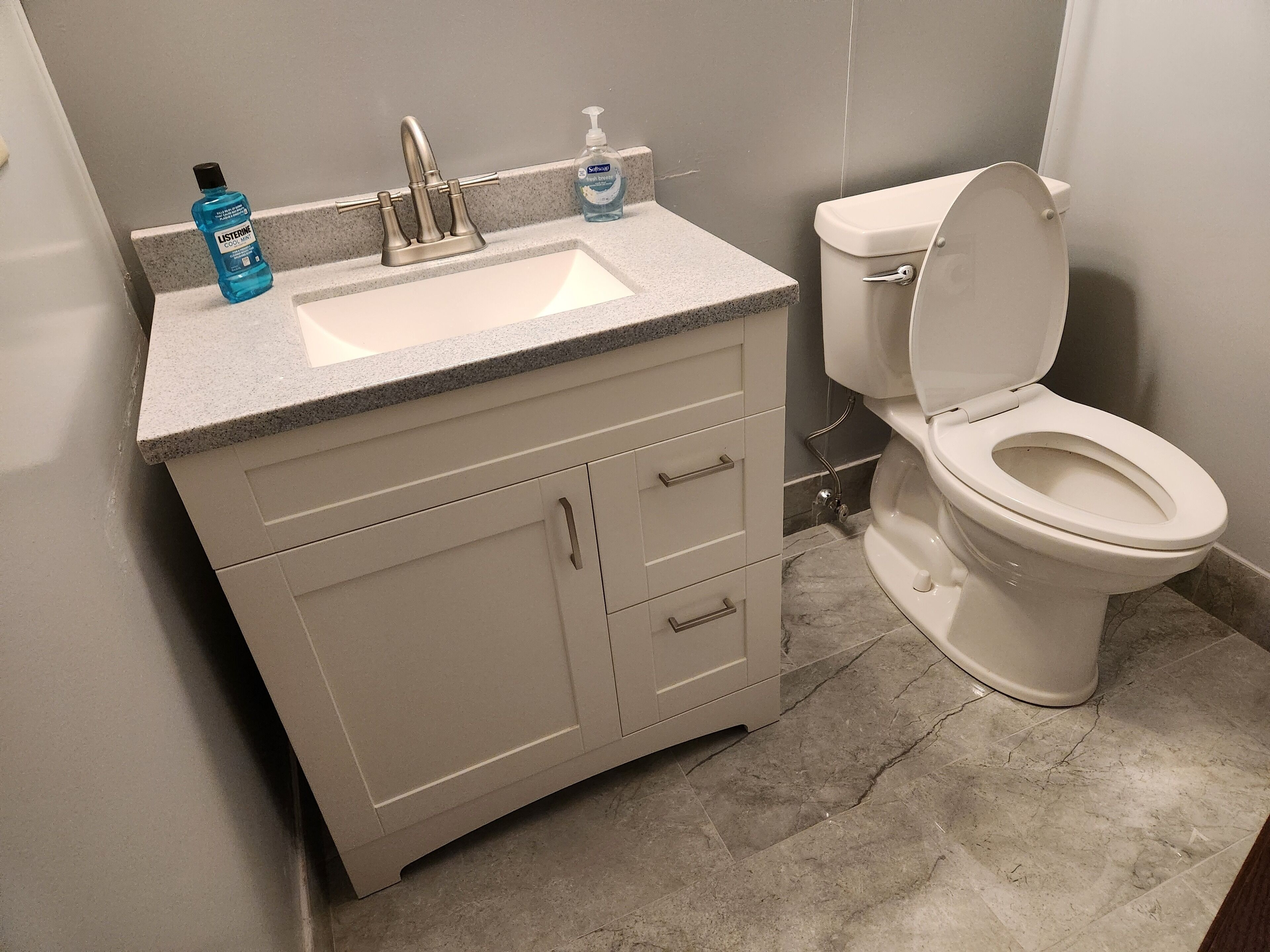 Une salle de bain avec un lavabo, un robinet et des toilettes, tous de couleur blanche. On peut voir deux flacons de savon pour les mains posés sur le lavabo.