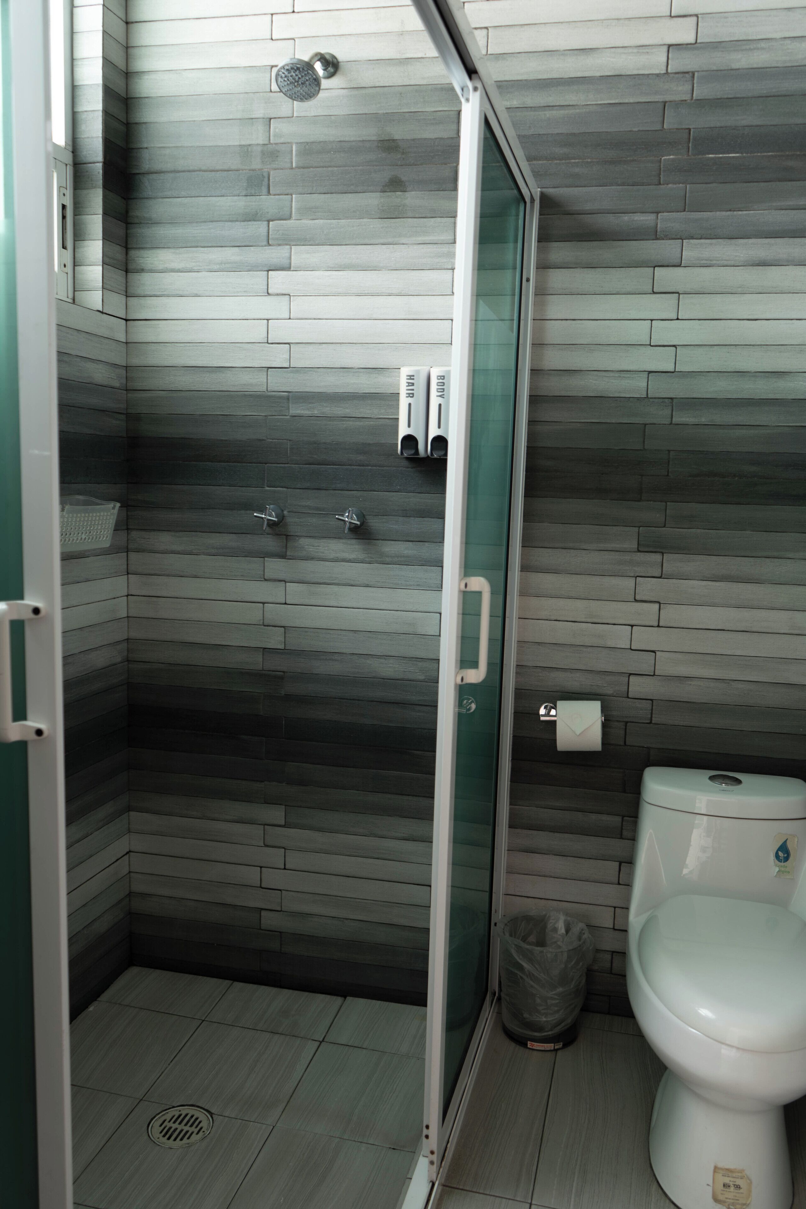 Une salle de bain équipée d’une douche, de toilettes et d’une poubelle.