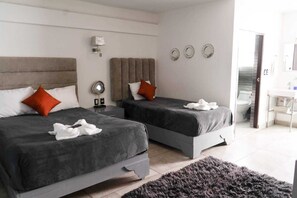 A modern hotel room with two beds, a small bedside table, a lamp, and a view of the bathroom.