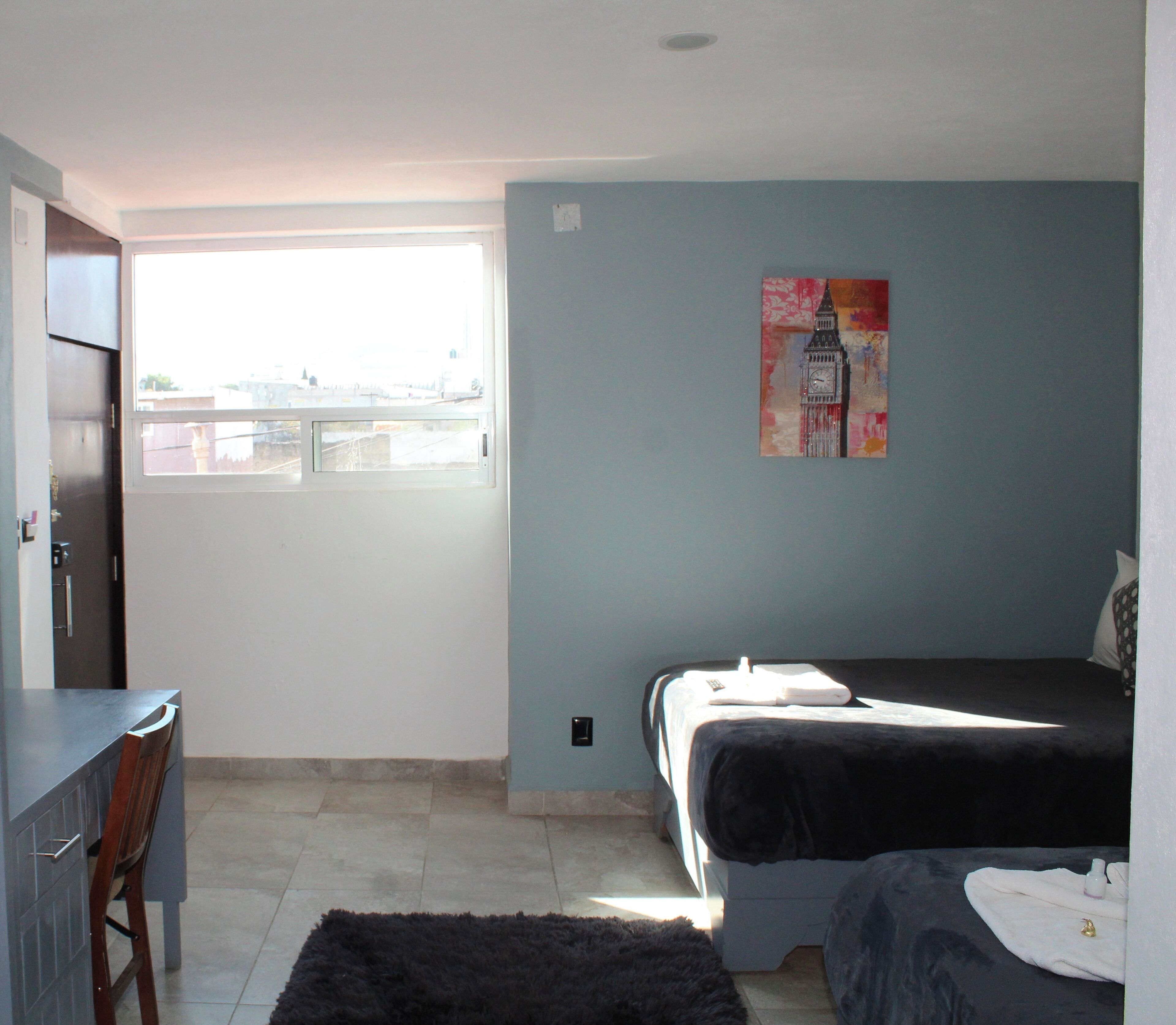 A bedroom with a bed, a desk, and a window.