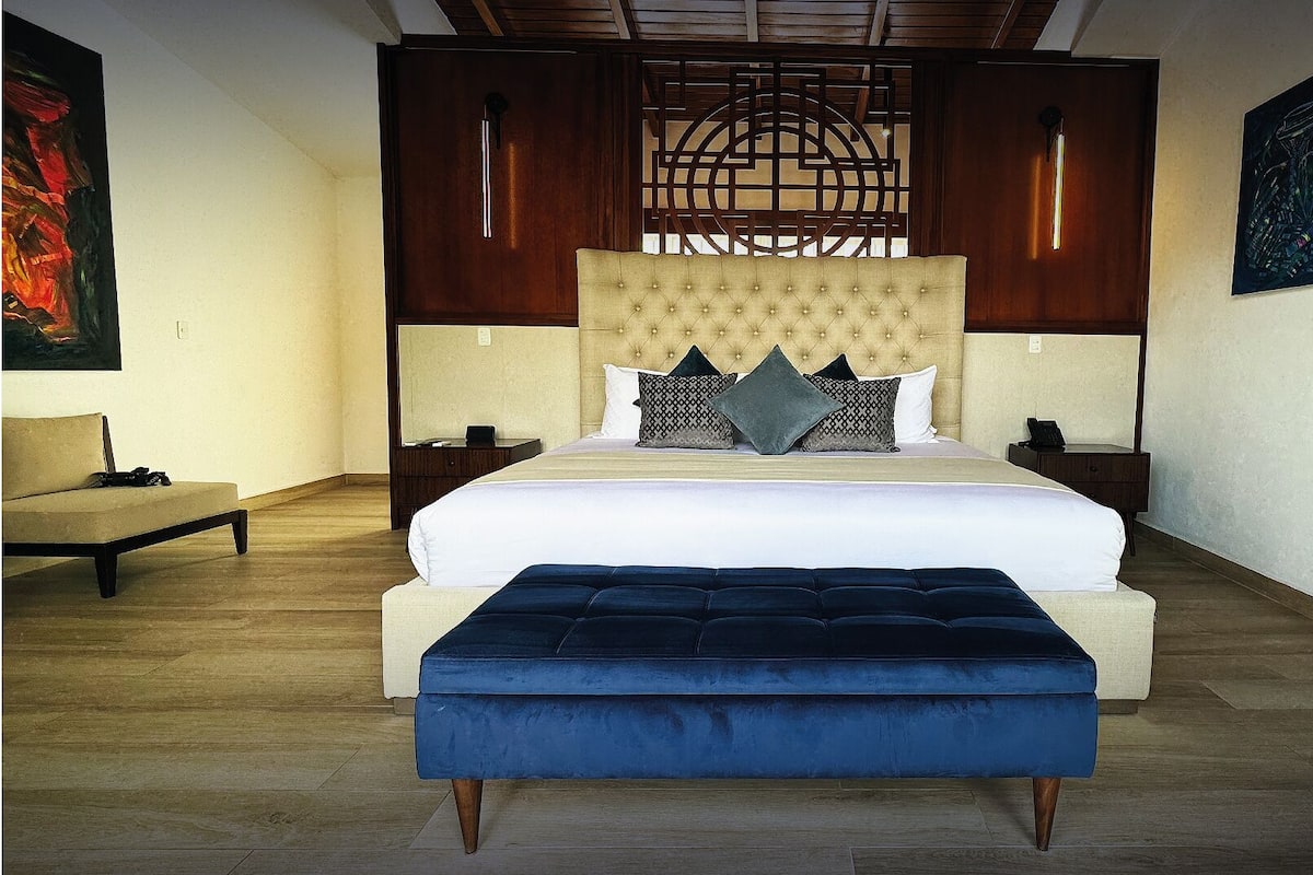 A spacious bedroom with a large bed, a wooden headboard, and a blue upholstered bench.