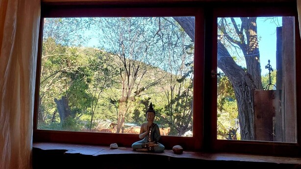 A statue of a seated figure on a windowsill with a view of trees and a hill outside.