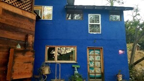 A two-story house with a blue exterior, a wooden porch, and a front door with a decorative glass panel.