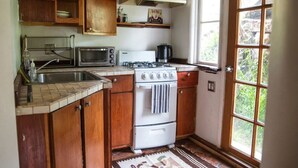 A kitchen with wooden cabinets, a white stove, a microwave, and a window with a view of greenery.