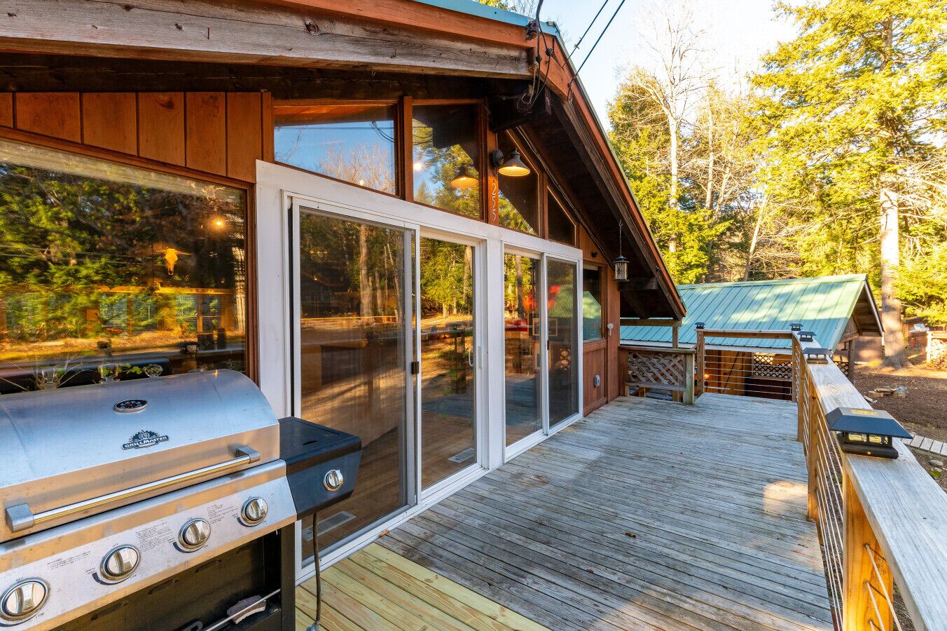 A wooden deck with a grill and sliding glass doors leading to an outdoor area.