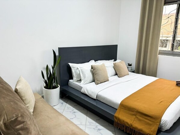 Une chambre à coucher moderne avec un lit, une table de chevet, une plante en pot et une fenêtre avec des rideaux.