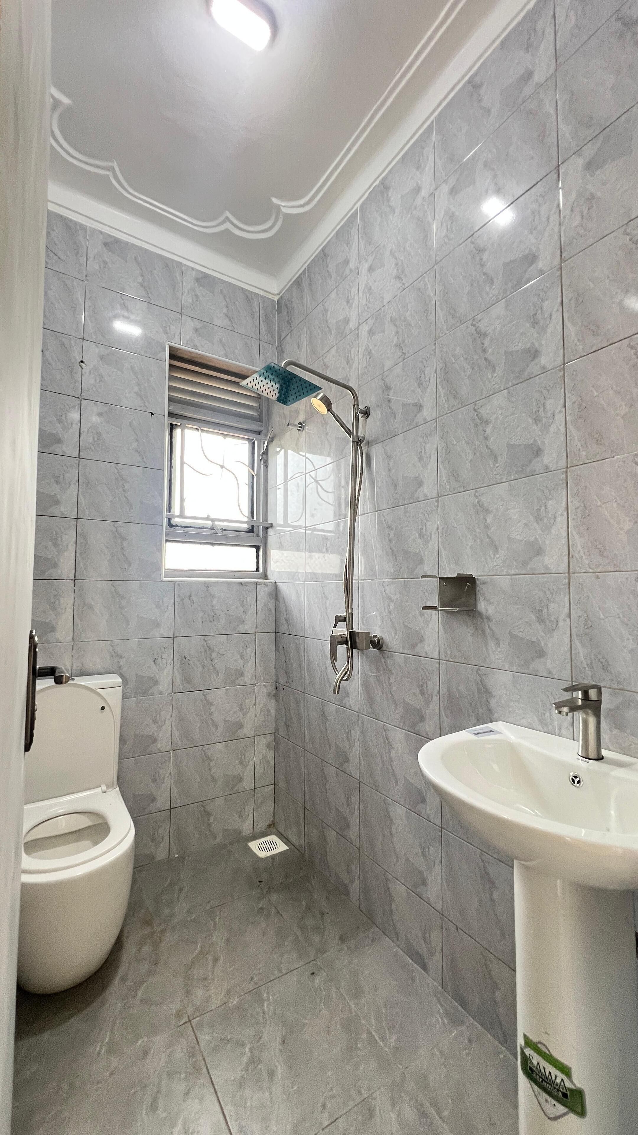 A bathroom with a toilet, a shower with a handheld showerhead, a sink, and a window.