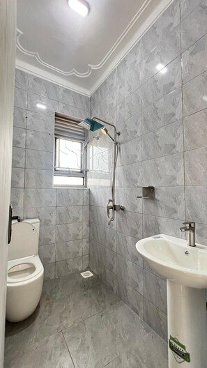 Une salle de bain comprenant des toilettes, une douche avec un pommeau de douche amovible, un lavabo et une fenêtre.