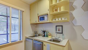A compact kitchen with a built-in dishwasher, a microwave, and a sink. There are cabinets above the counter and a hexagonal tile backsplash.