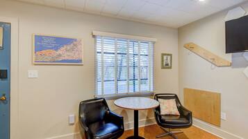 A room with two black leather chairs, a small round table, a window with blinds, a map on the wall, and a mounted TV.