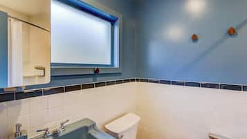 A bathroom with a blue wall, white tiles, a window above the sink, and a toilet.
