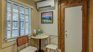 Una habitació petita amb finestra, taula i cadires, aire condicionat i una porta.