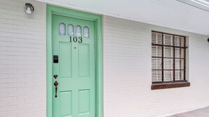 A green door with the number 103, a window with shutters, and a white brick wall. - Historic Blue Ridge Tourist Court - Queen Plus (Boone)