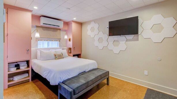 A bedroom with a bed, a bench, a wardrobe, a TV, and hexagonal wall decor. - Historic Blue Ridge Tourist Court - Queen Plus (Boone)