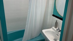 A bathroom with a white tiled wall, a turquoise bathtub, a white sink with a mirror above it, and a shower curtain. - Historic Blue Ridge Tourist Court - One Bathroom Suite (Boone)