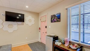 A modern kitchen with a flat-screen TV, hexagonal wall decor, a pink door, and a window with blinds. - Historic Blue Ridge Tourist Court - The Whole Tourist Court (Boone)