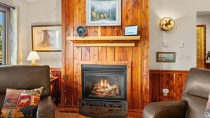 A cozy living room with a fireplace, wooden paneling, and leather furniture. - Moose Horn Lodge- A Clean Cabin for Families, Wedding Goers & Montana Adventures (Livingston)