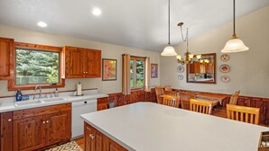 A kitchen with wooden cabinets, a large island, and a dining area with wooden chairs. - Moose Horn Lodge- A Clean Cabin for Families, Wedding Goers & Montana Adventures (Livingston)