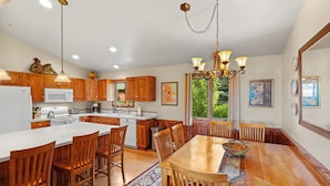 A spacious kitchen with wooden cabinets, a large island, and a dining area with wooden chairs and a table. - Moose Horn Lodge- A Clean Cabin for Families, Wedding Goers & Montana Adventures (Livingston)