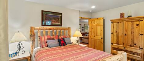 A bedroom with a wooden bed frame, a patterned bedspread, two bedside lamps, a nightstand, and a wardrobe.
