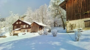Puinen mökki, jonka alla on kivestä rakennettu pohja, ja jonka ympärillä on lumipeitteisiä puita ja kirkas taivas.