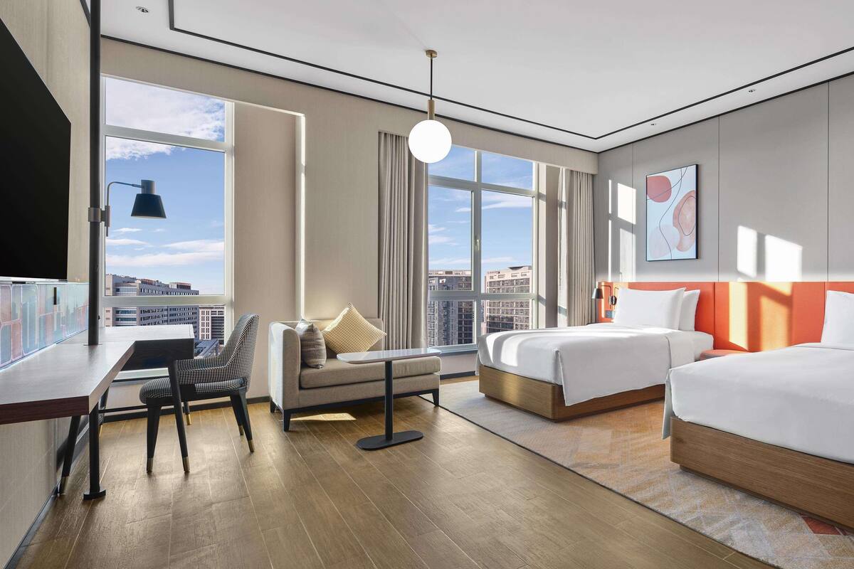 Une chambre d’hôtel moderne dotée d’une grande fenêtre, d’un lit, d’un canapé, d’un bureau et d’une chaise.