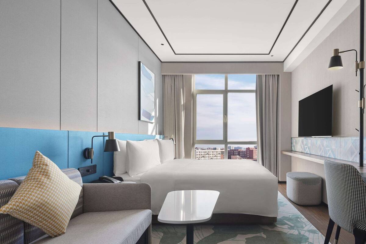 Une chambre d’hôtel moderne équipée d’un lit, d’un canapé, d’une petite table, d’une télévision et d’une fenêtre donnant sur la ville.