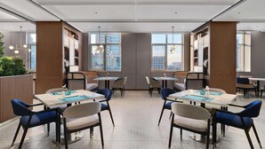 Un'area ristorazione moderna con diversi tavoli e sedie, ampie finestre con vista sulla città e un design pulito e contemporaneo.