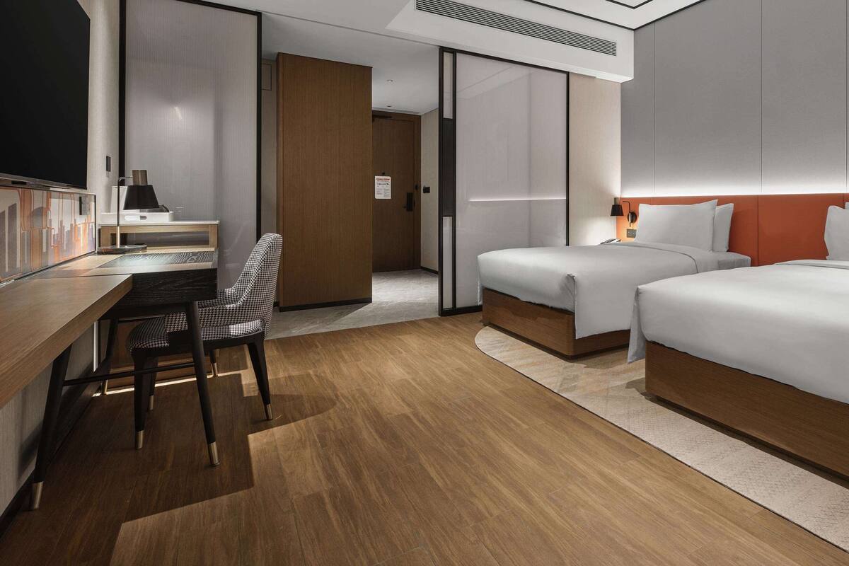 Une chambre d’hôtel moderne avec un bureau en bois, deux lits, une chaise et une grande fenêtre.