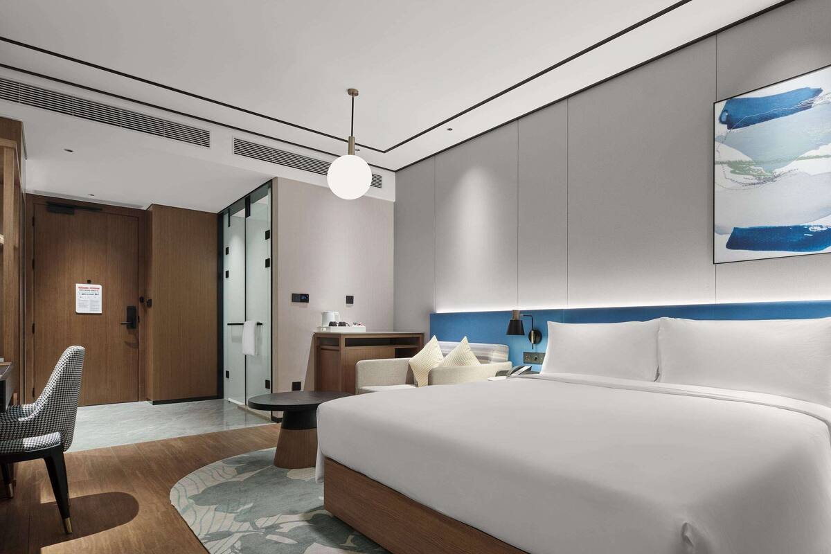 Une chambre d’hôtel moderne, dotée d’un grand lit, d’un bureau, d’une chaise et d’une salle de bain avec une porte en verre.