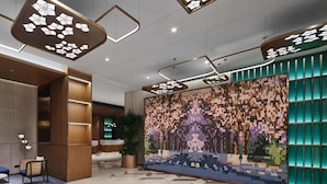 Una hall moderna con luci a soffitto geometriche, una reception, una zona relax e una parete con mosaico colorato.