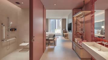 A modern bathroom with a shower, toilet, and sink. There is a dining area with a table and chairs, and a large window providing natural light.