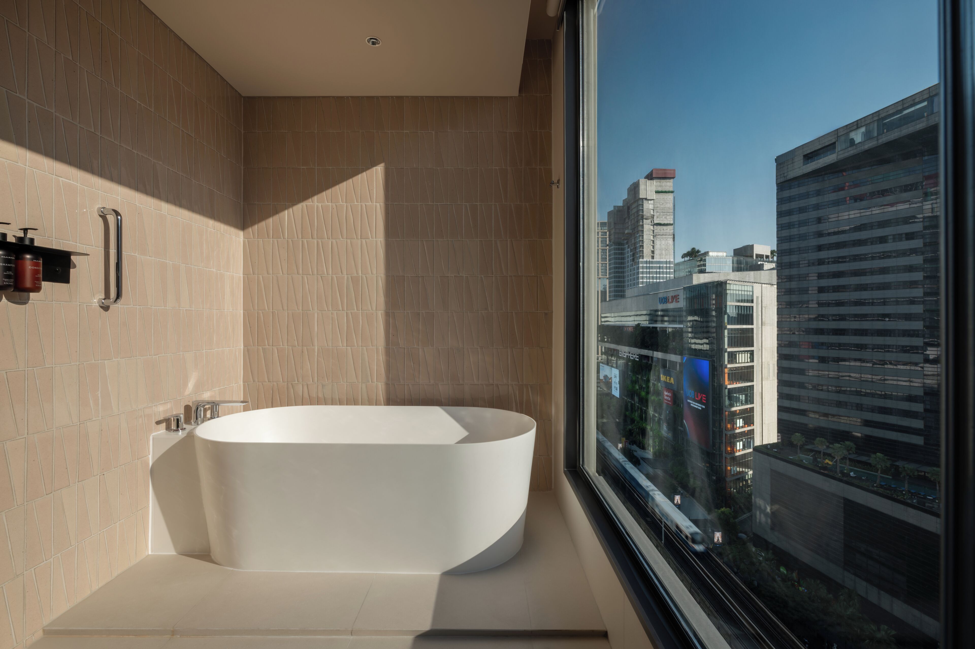 A modern bathroom with a freestanding bathtub, a handrail, and a window overlooking a cityscape.