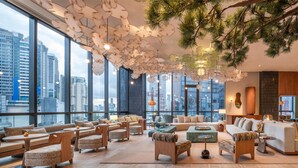 A modern interior with large windows, a cozy seating area, and a bar. - KROMO Bangkok, Curio Collection by Hilton (Bangkok)