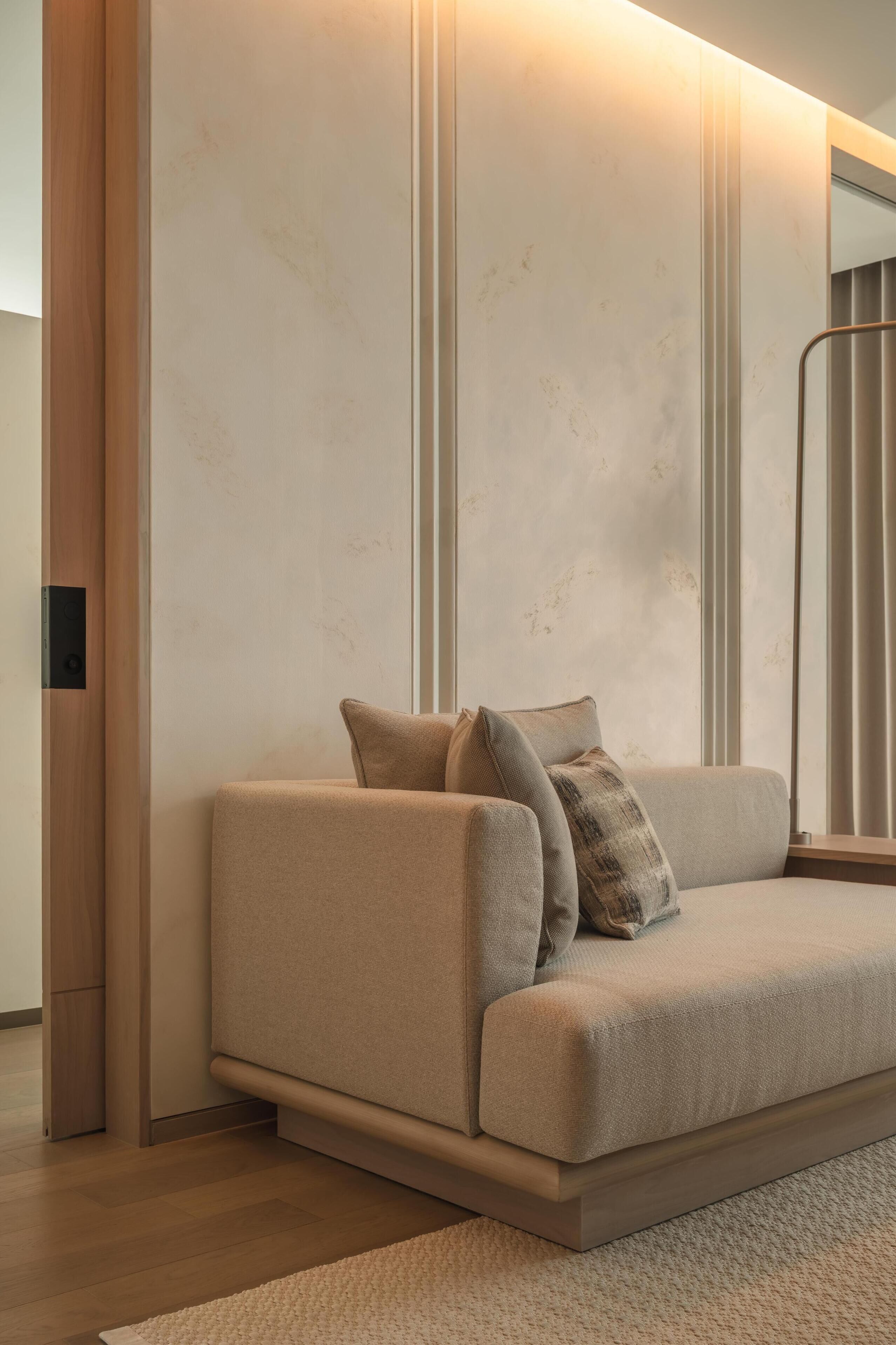 Una sala de estar moderna con un sofá color crema, piso de madera y un ventanal con persianas verticales.