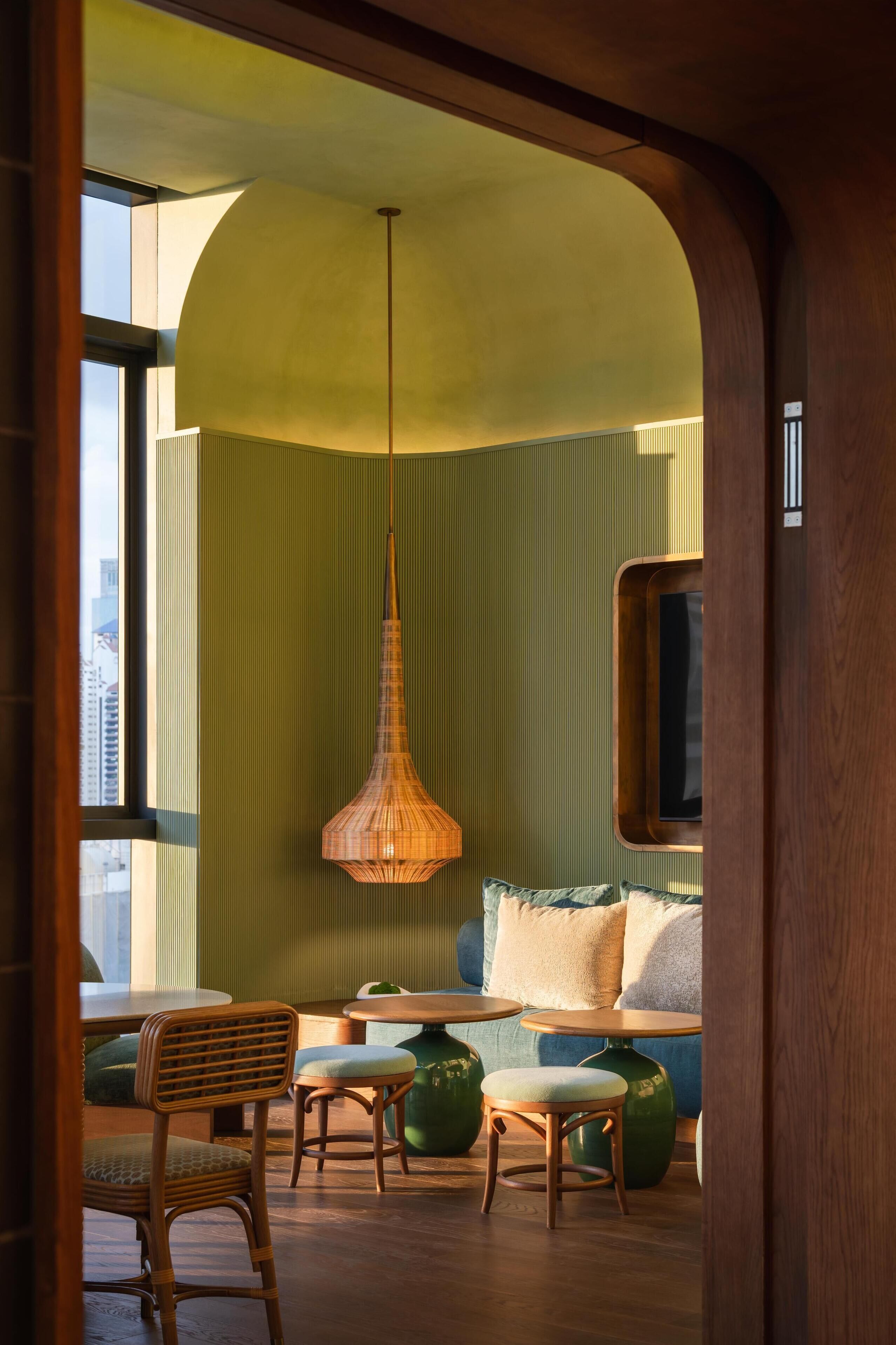 A cozy interior with a curved ceiling, a hanging light fixture, a sofa with cushions, and a dining area with chairs and a table.