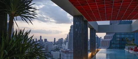 Una piscina moderna en la azotea con vista a la ciudad, destacada por un diseño arquitectónico único con techo iluminado en rojo y un edificio de cristal al fondo.