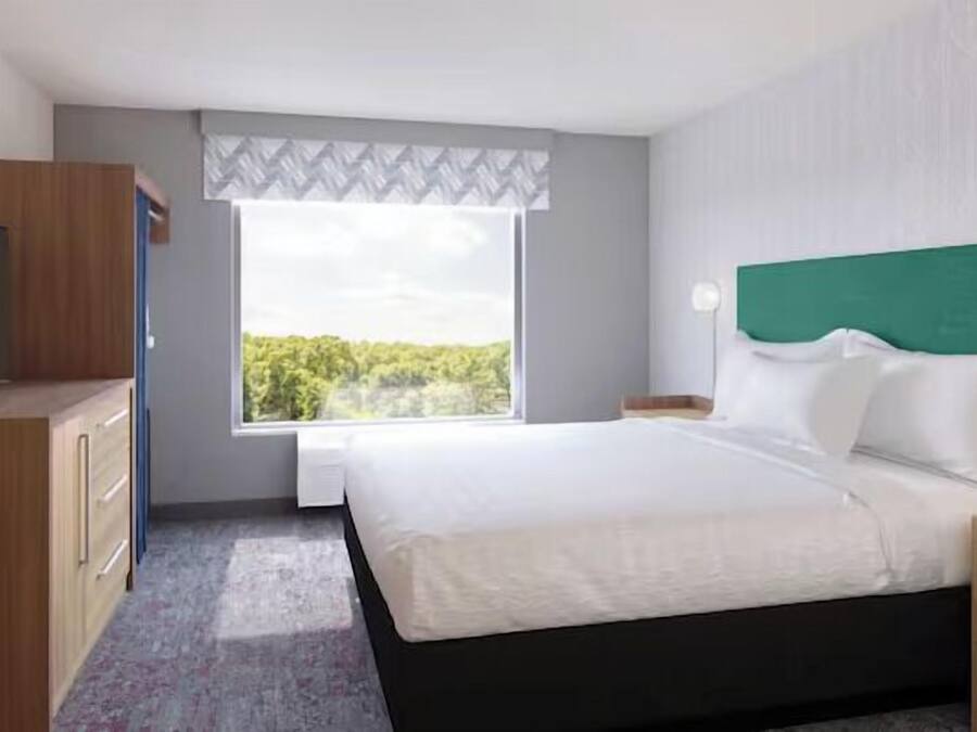 Ein Hotelzimmer mit Bett, Fernseher, Schreibtisch und Fenster mit Blick auf Grünfläche.