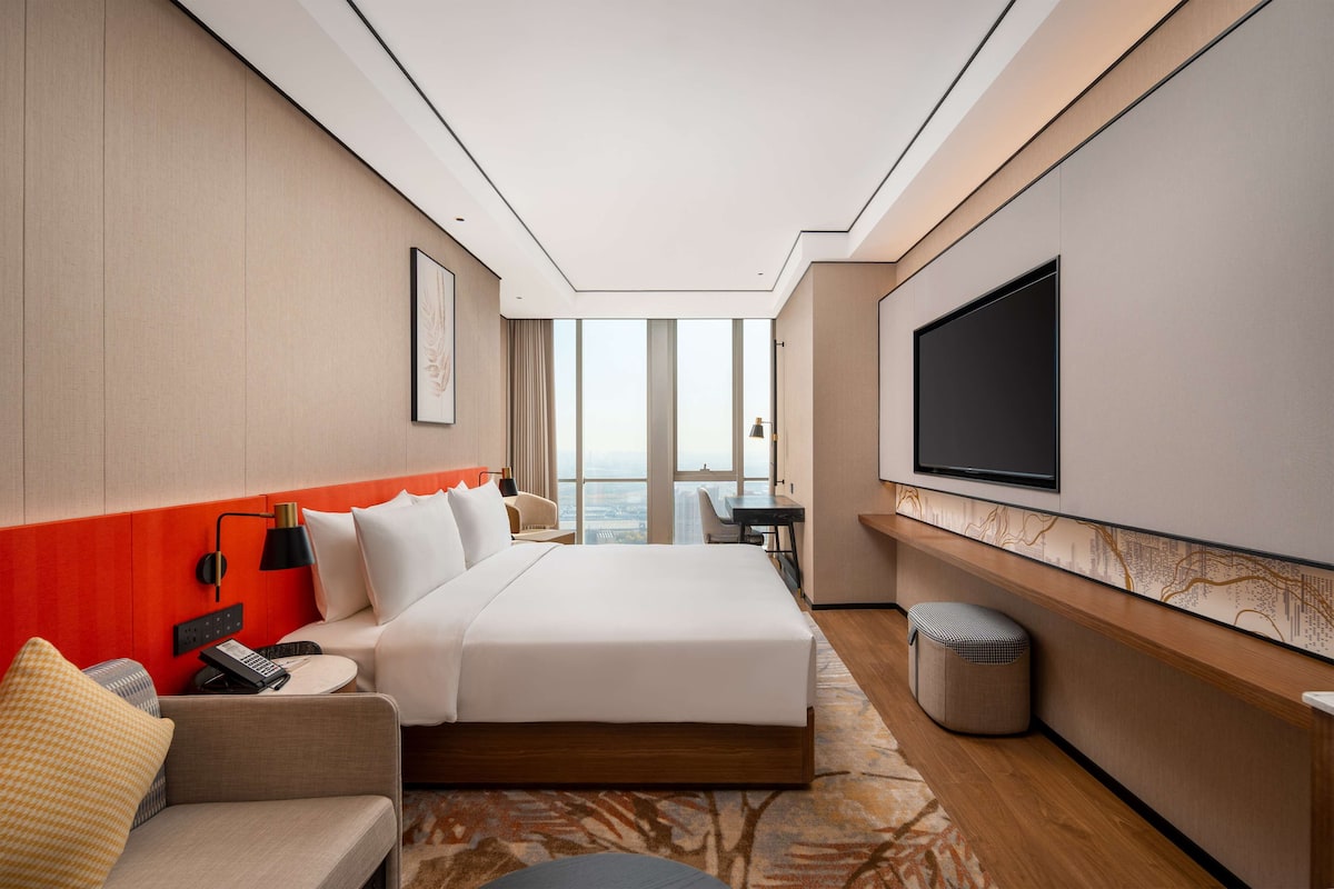 A modern hotel room with a large bed, a sofa, a TV, and a view of the city.
