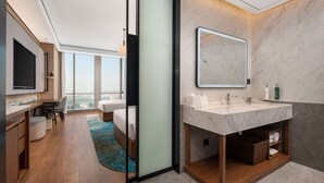 A modern hotel room with a large window, a flat-screen TV, a wooden dining table, and a large bathroom with a marble sink and mirror. - Hilton Garden Inn Hefei Feixi (Hefei)