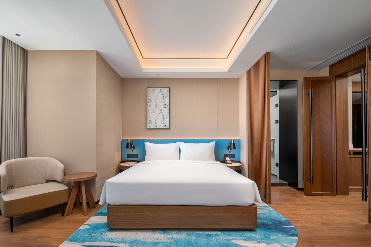 A modern hotel room with a large bed, a sofa, a small round table, and a ceiling light fixture.