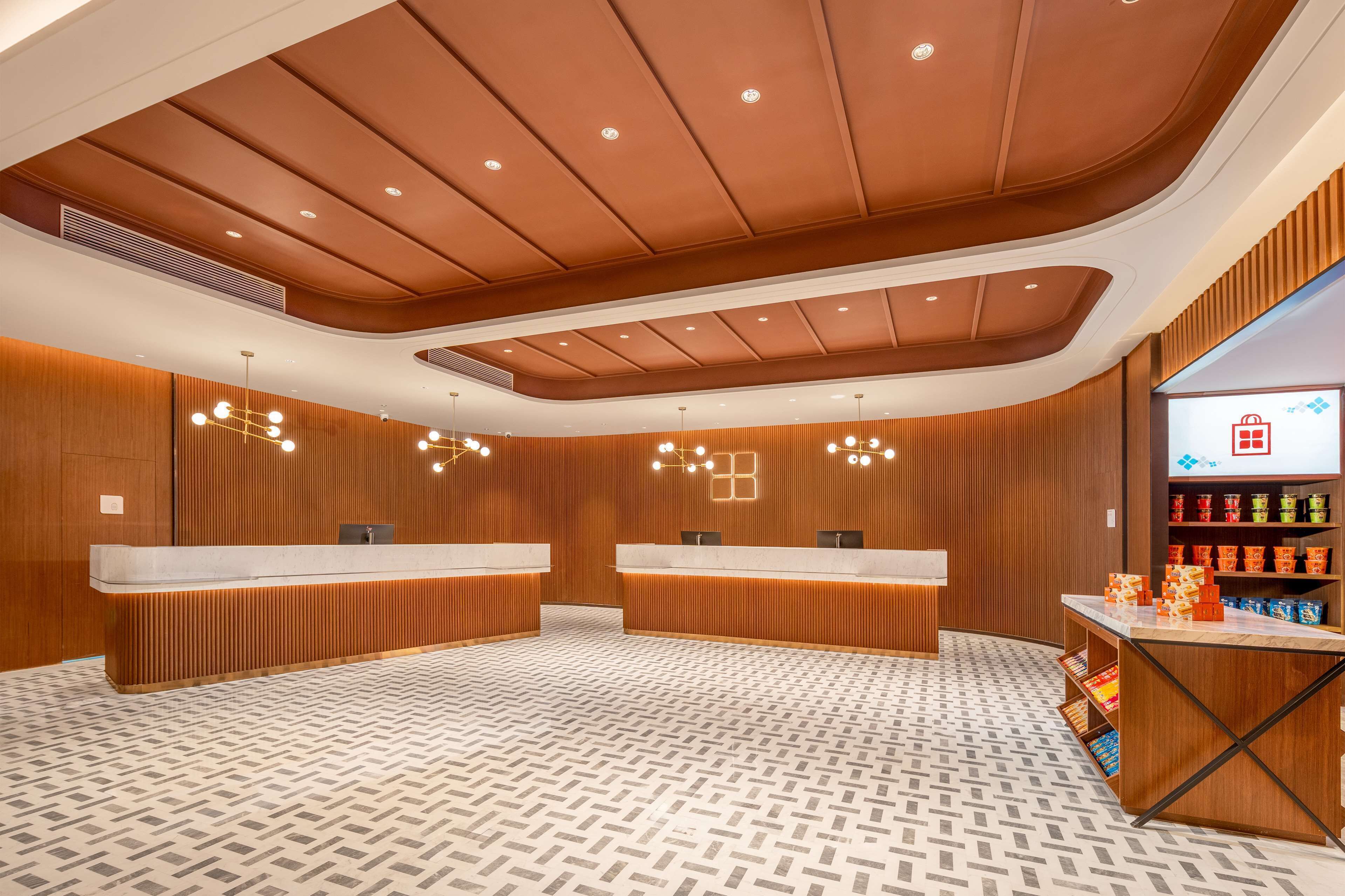 Un espace d’accueil moderne avec un lambris en bois, deux comptoirs de réception, un revêtement de sol à motifs et un présentoir de collations.