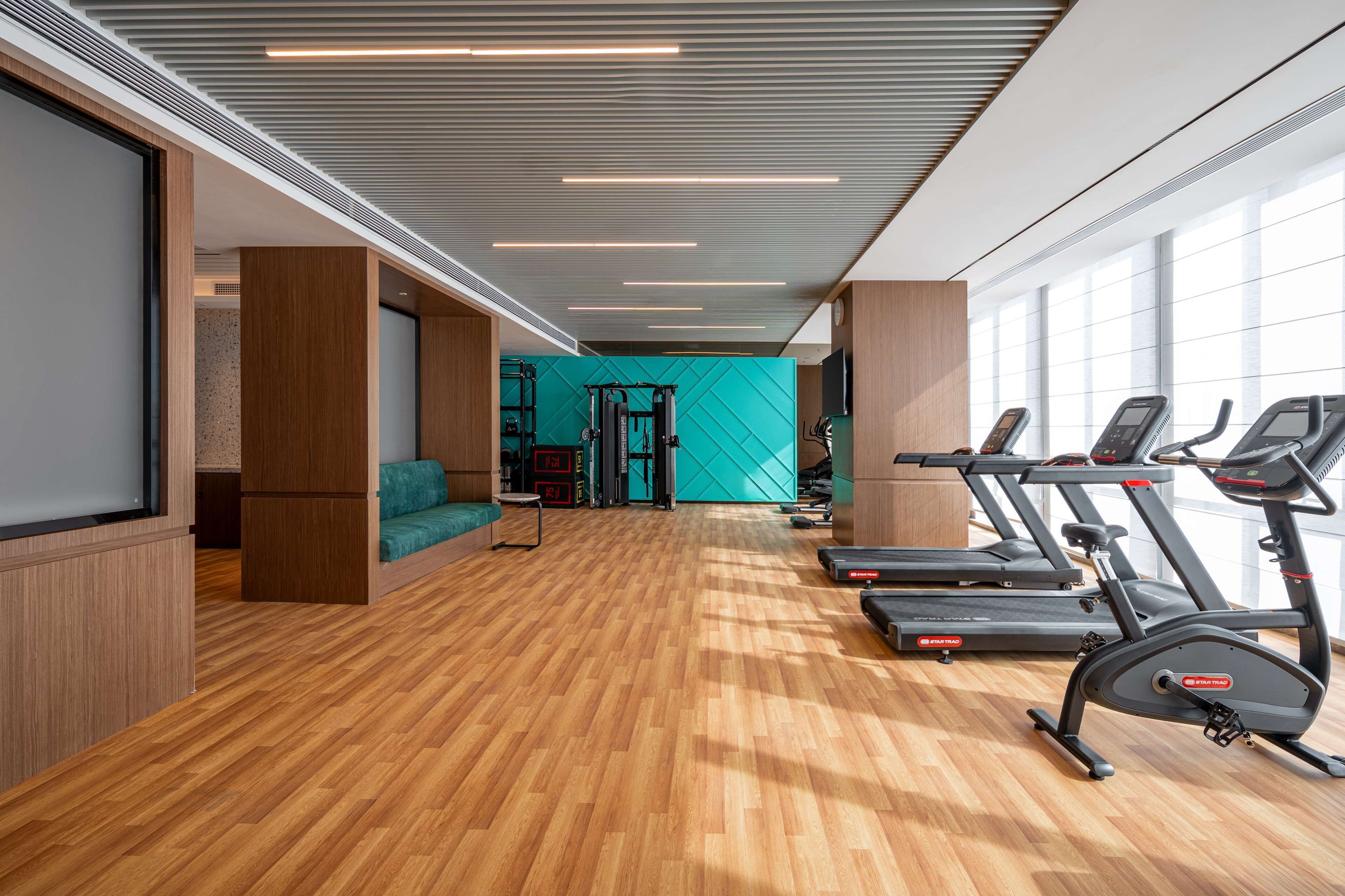 A modern gym with wooden flooring, exercise equipment, and large windows.