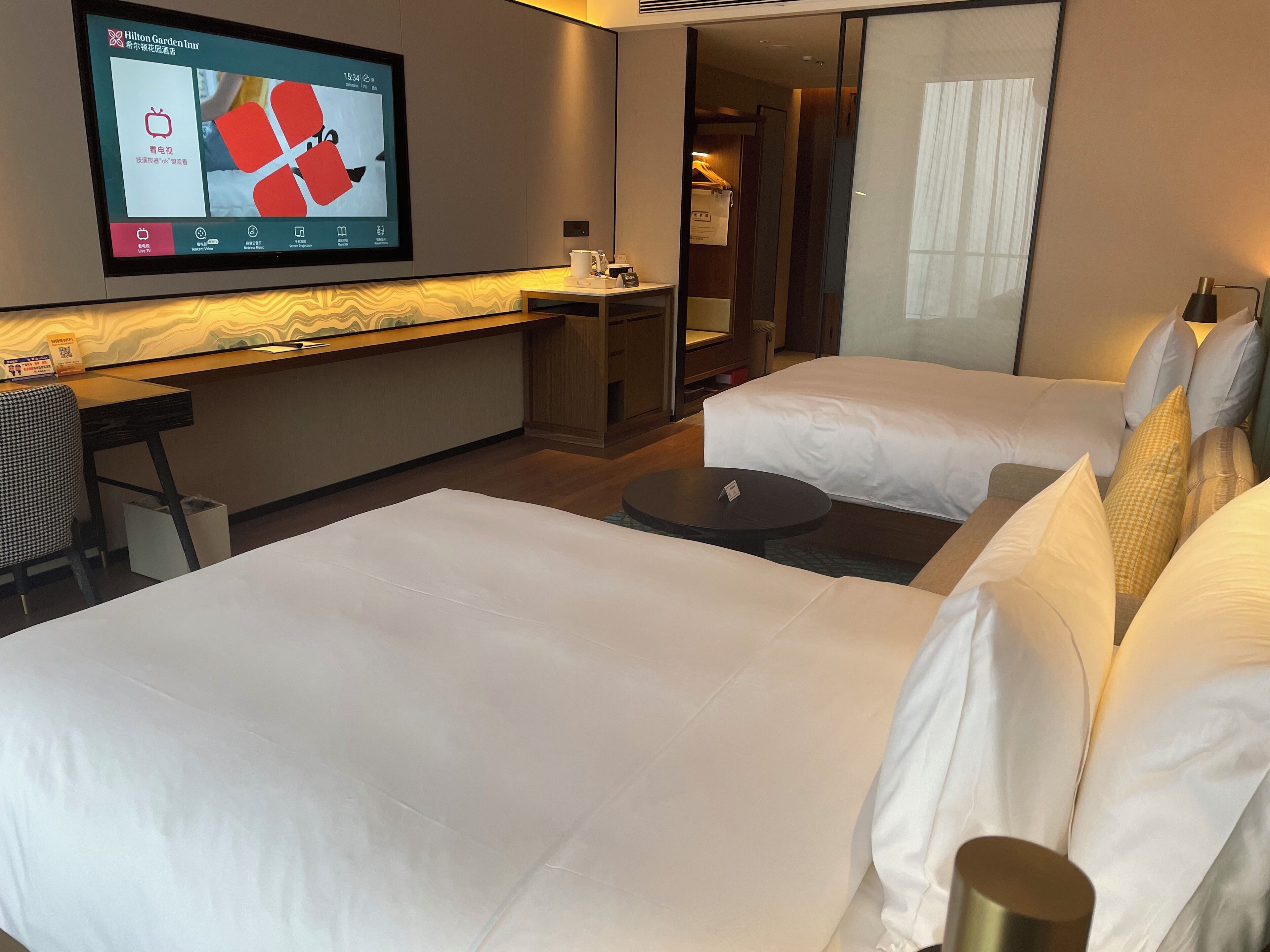 A hotel room with two beds, a desk, a TV mounted on the wall, and a closet.