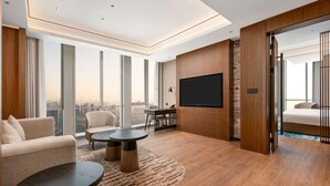 A modern hotel room with a large window, a flat-screen TV, a sofa, a coffee table, and a desk with a chair. - Hilton Garden Inn Hefei Feixi (Hefei)
