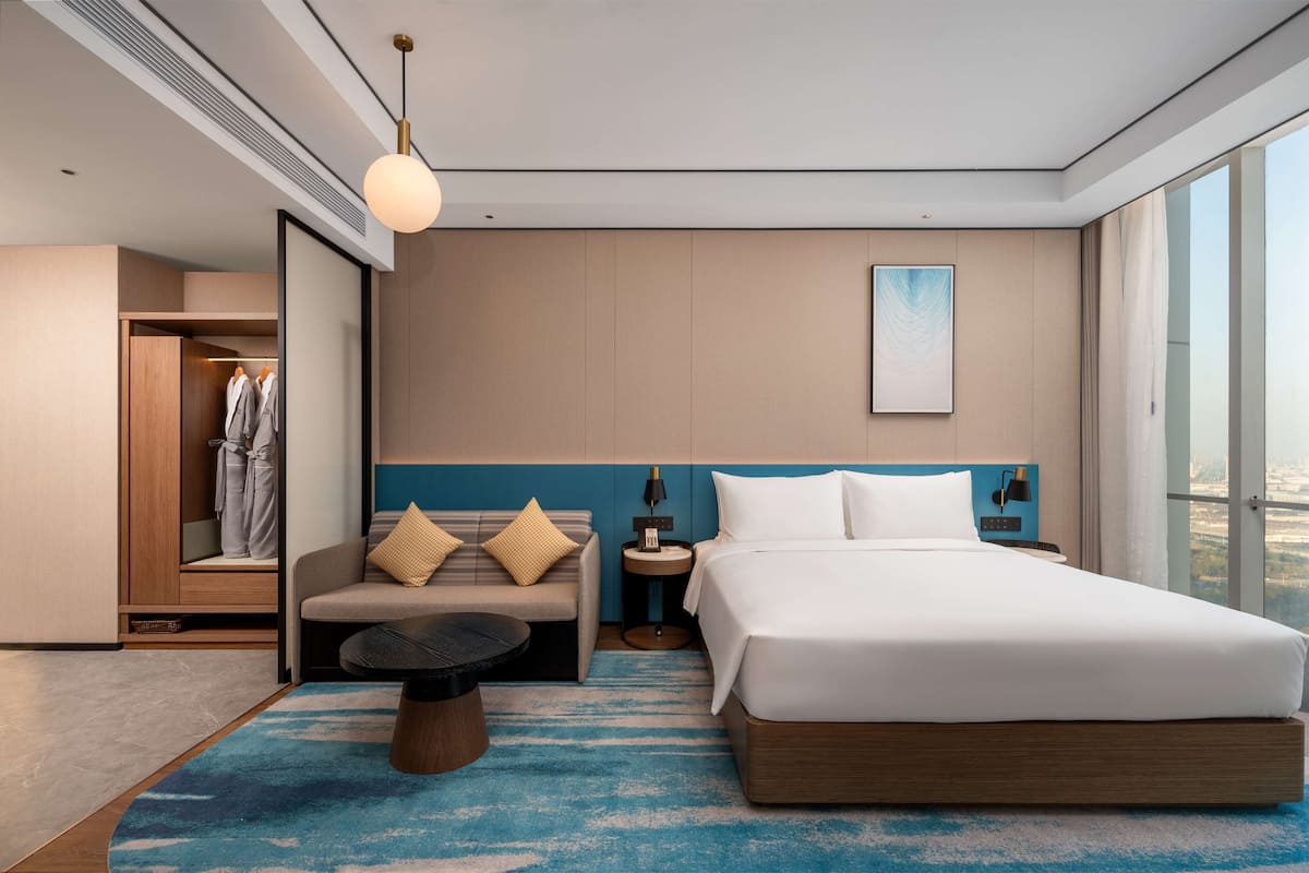 A modern hotel room with a large bed, a sofa, a small table, and a view of the city.